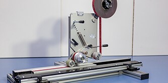 Image of a machine for applying 3M™ VHB Tape to a piece of square tubing pushed through the guides
