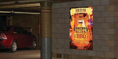 A poster in a dark underground garage with flames advertising a BBQ and shining at night using 3M reflective films.
