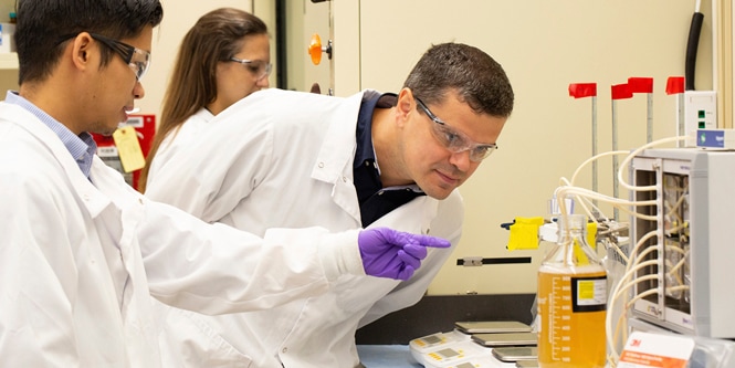 Scientists in lab coats inspecting fluid
