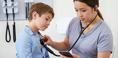 Clinician auscultating a boy’s chest while looking at phone app
