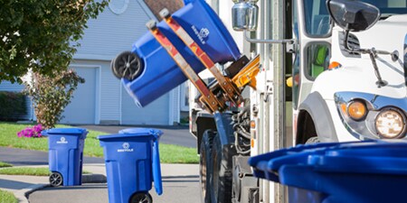 A blue recycling bin is being lifted to a recycling truck.

