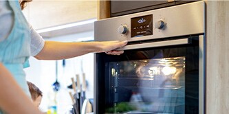 A person wearing an apron who is about to open the door of an oven
