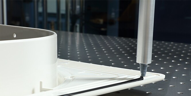 Image of a dispenser tip applying adhesive around the edge of a moulded plastic form
