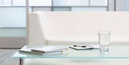 3MTM Glass Finishes cover windows in a hotel lobby where a white couch and newspapers invite travellers to rest.
