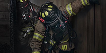 A firefighter in firefighter personal protective equipment walking through a smoky building
