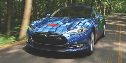 A Tesla Model S zooming down a highway, wrapped in blue 3M Envision print wrap film LX480mC with a 3m logo on the hood of the car.
