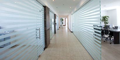 A long office hallway with glass walls has striped wall wraps that provide privacy and a sleek look.
