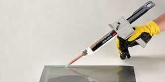 Image of a worker using a hand applicator to apply adhesive to a piece of plastic
