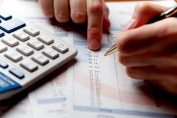 Close-up of hands using a calculator and pointing at a document with numbers, indicating financial analysis or data review.