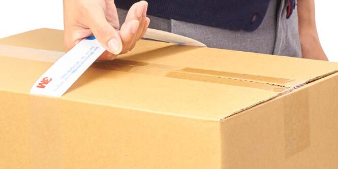 A close up of a person's hand holding a cardboard box by a handle.

