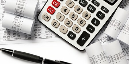 A calculator is surrounded by printed receipts and charts.
